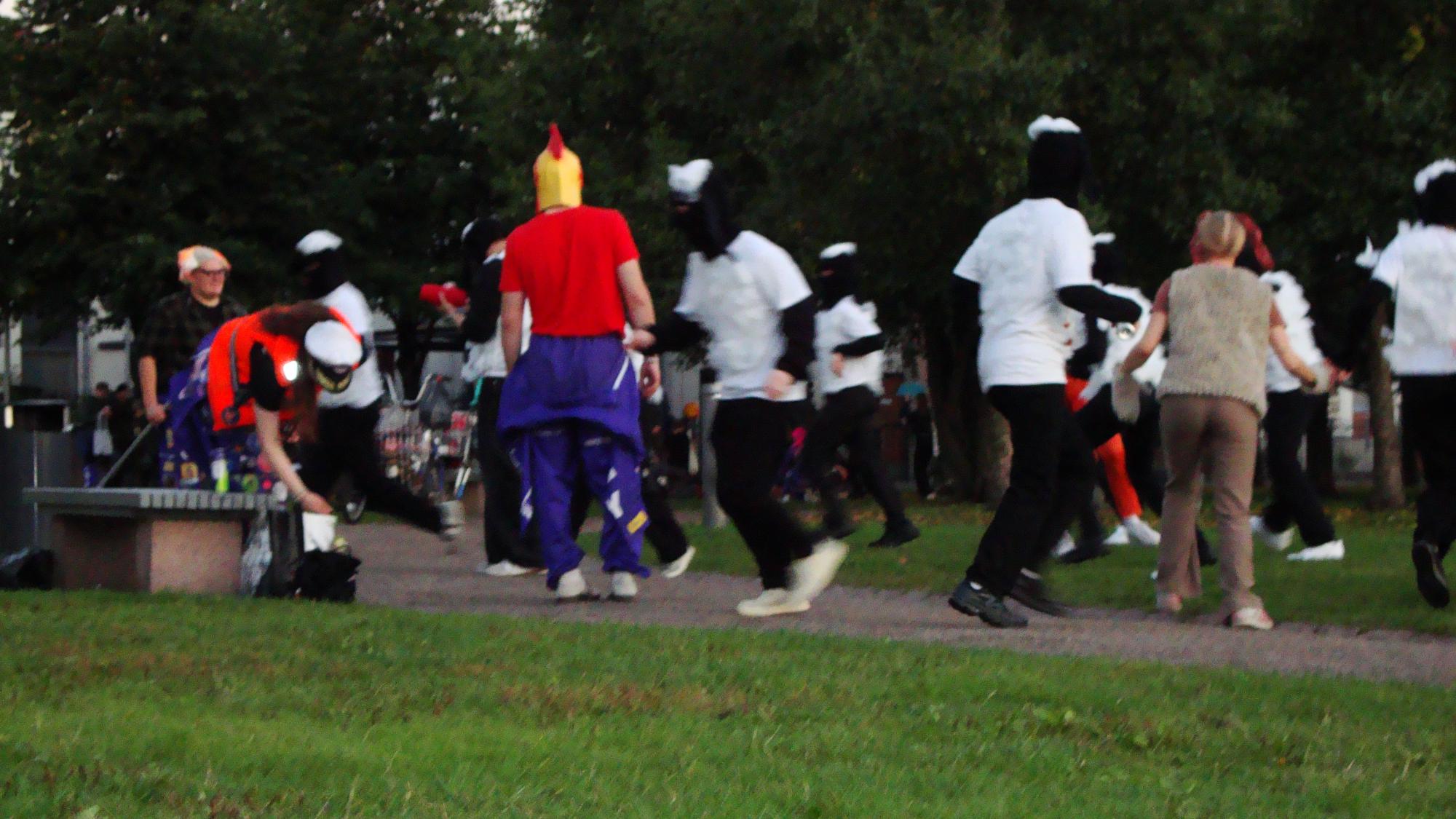 A group of students in colorful overalls are playing and socializing outdoors during a guild event in the park
