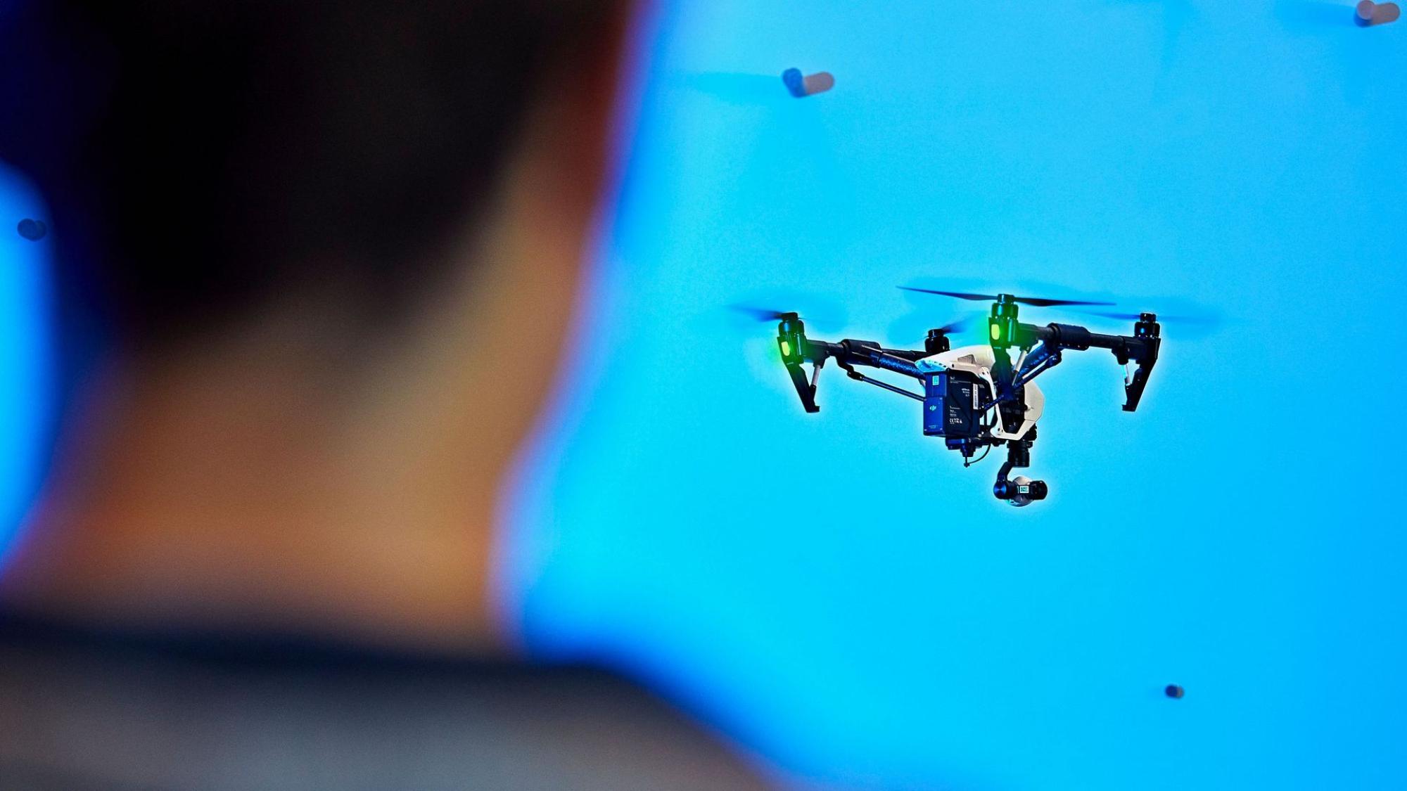A drone is flying in the air. A human figure is watching its movement..