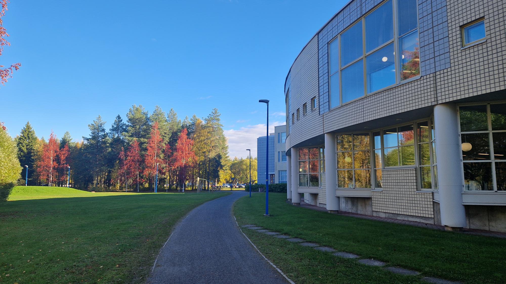Kuvassa Tiedekirjasto Pegasus ja syksyistä maisemaa: pyörätie ja metsikköä ruskan väreissä.