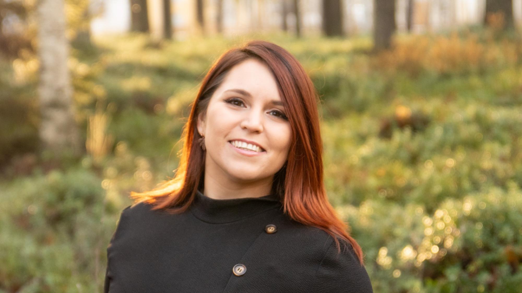 A portrait of Tamara Hoffman smiling with an autumn forest in the background