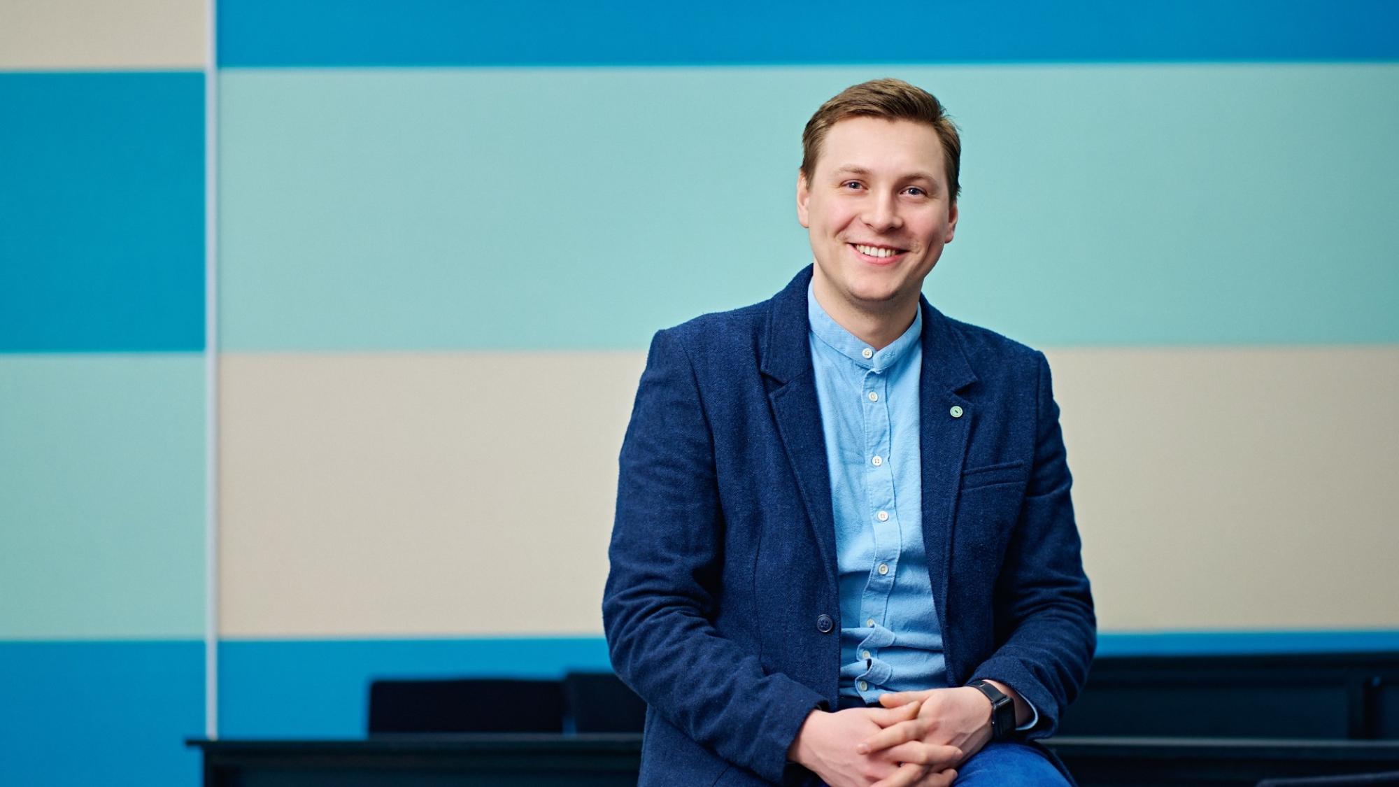 Researcher Filipp Temerov smiling in a portrait with a light blue patterned background