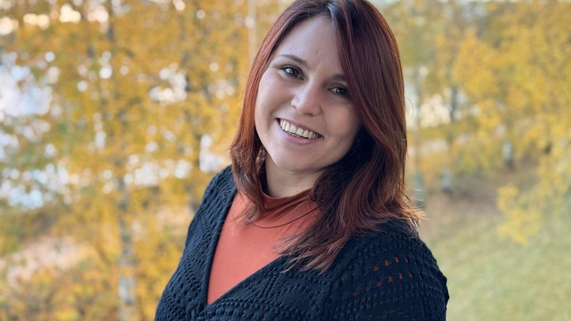 Tamara Hoffmann smiling in a portrait photo with yellow autumn trees in the background