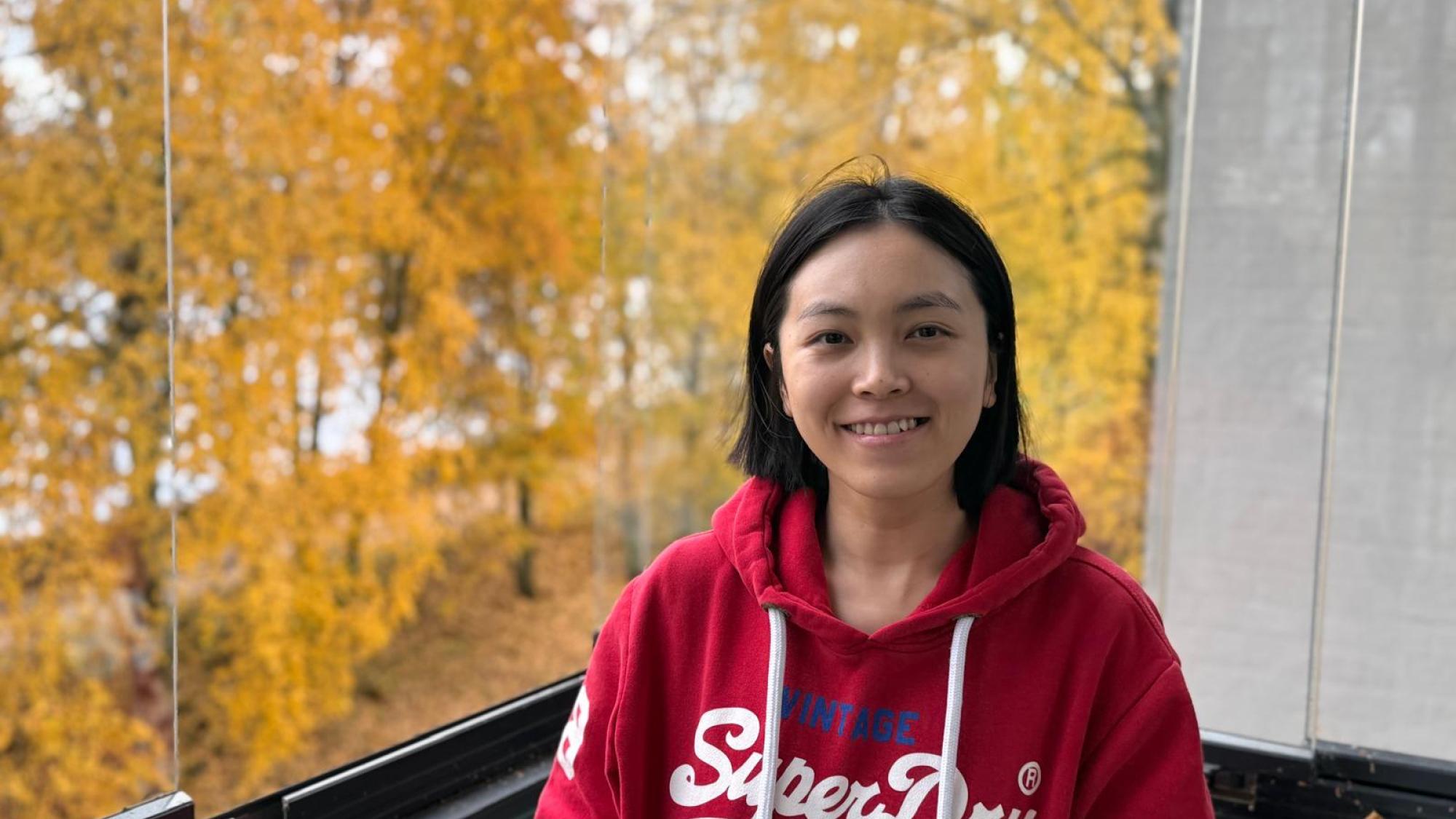 Ying Liao smiling in a portrait photo with yellow autumn trees in the background